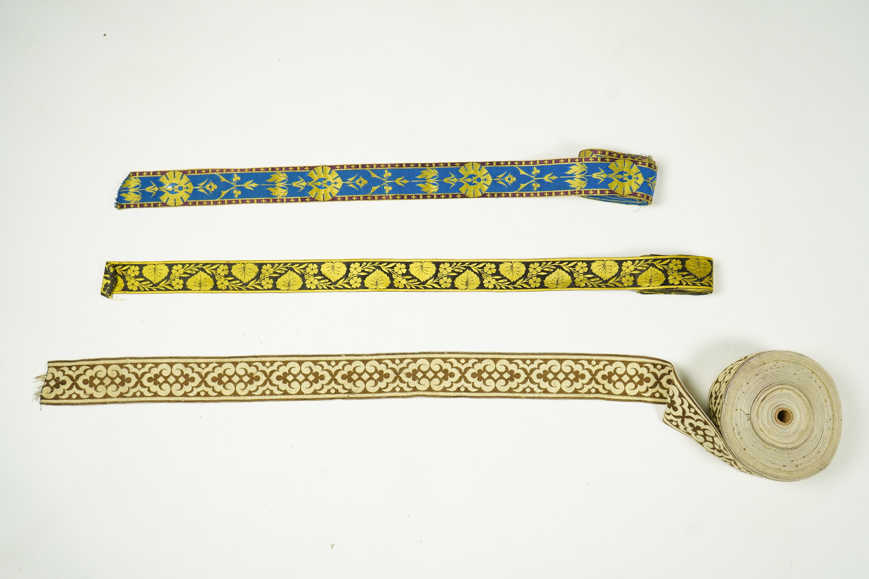 Three long lengths of late 19th century silk woven braiding. One woven in gold, turquoise and maroon silk, possibly for ecclesiastic use, in Christopher Dresser ‘style’ motifs, another in gold and black silk thread in a